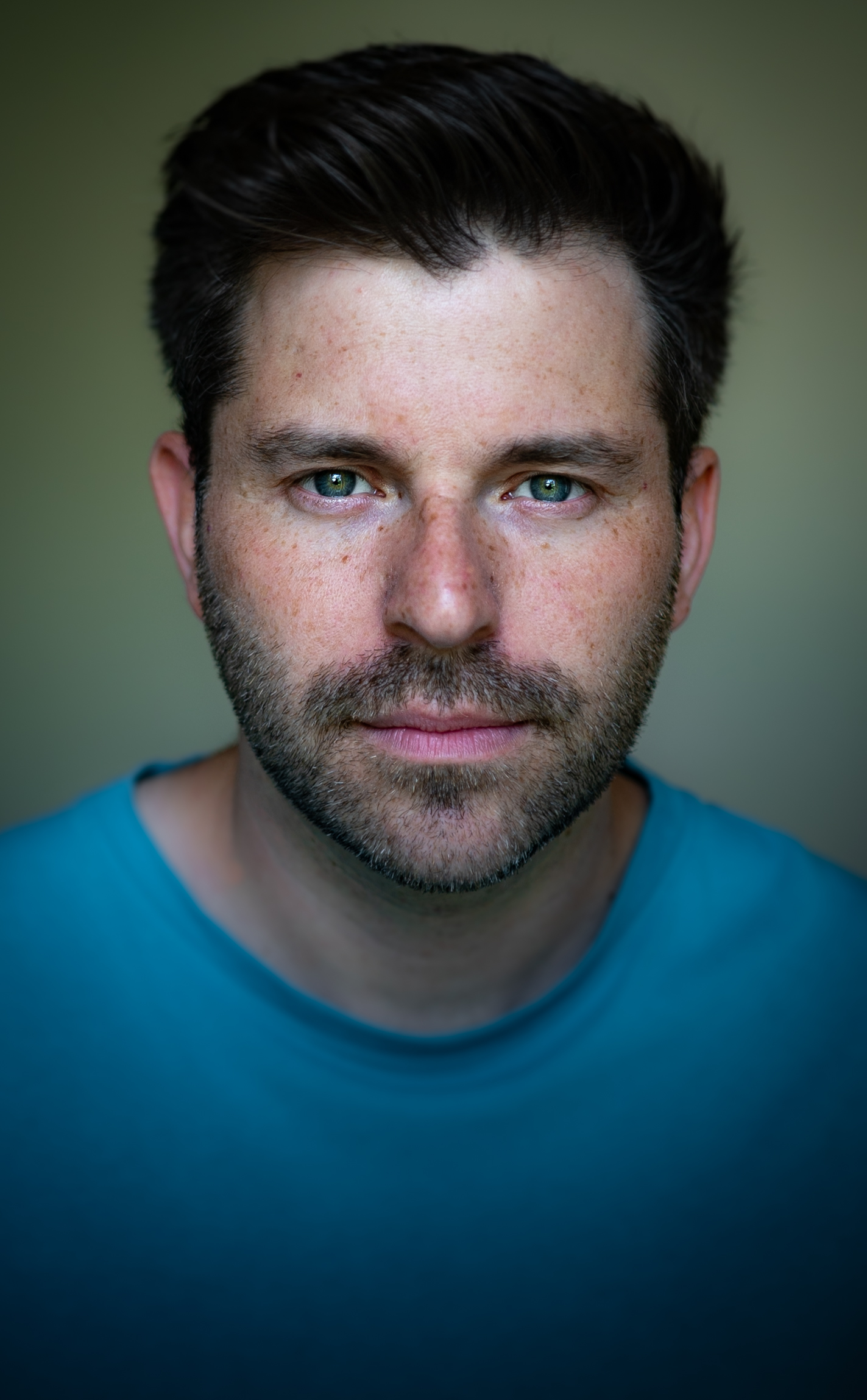 A headshot photo of Ned Bennett, a white man with dark brown hair, stubble and blue eyes.